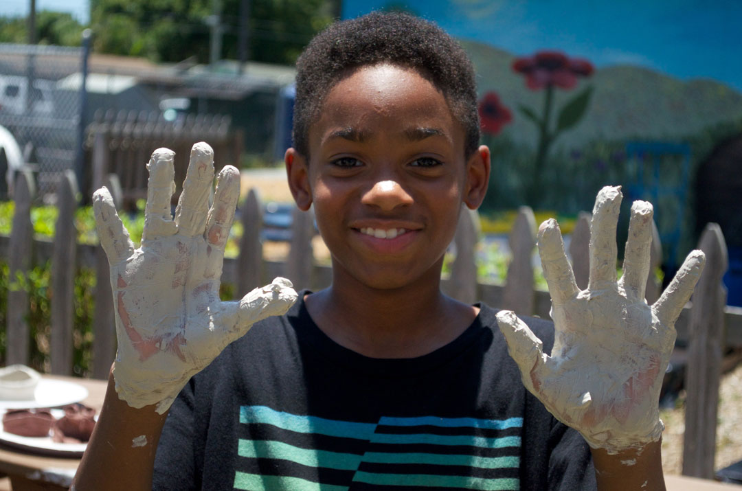 Young boy displays clay covered hands.
