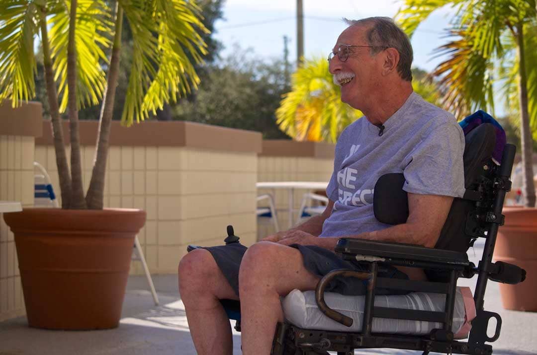 Smiling man in wheel chair relaxes on a sunny patio.