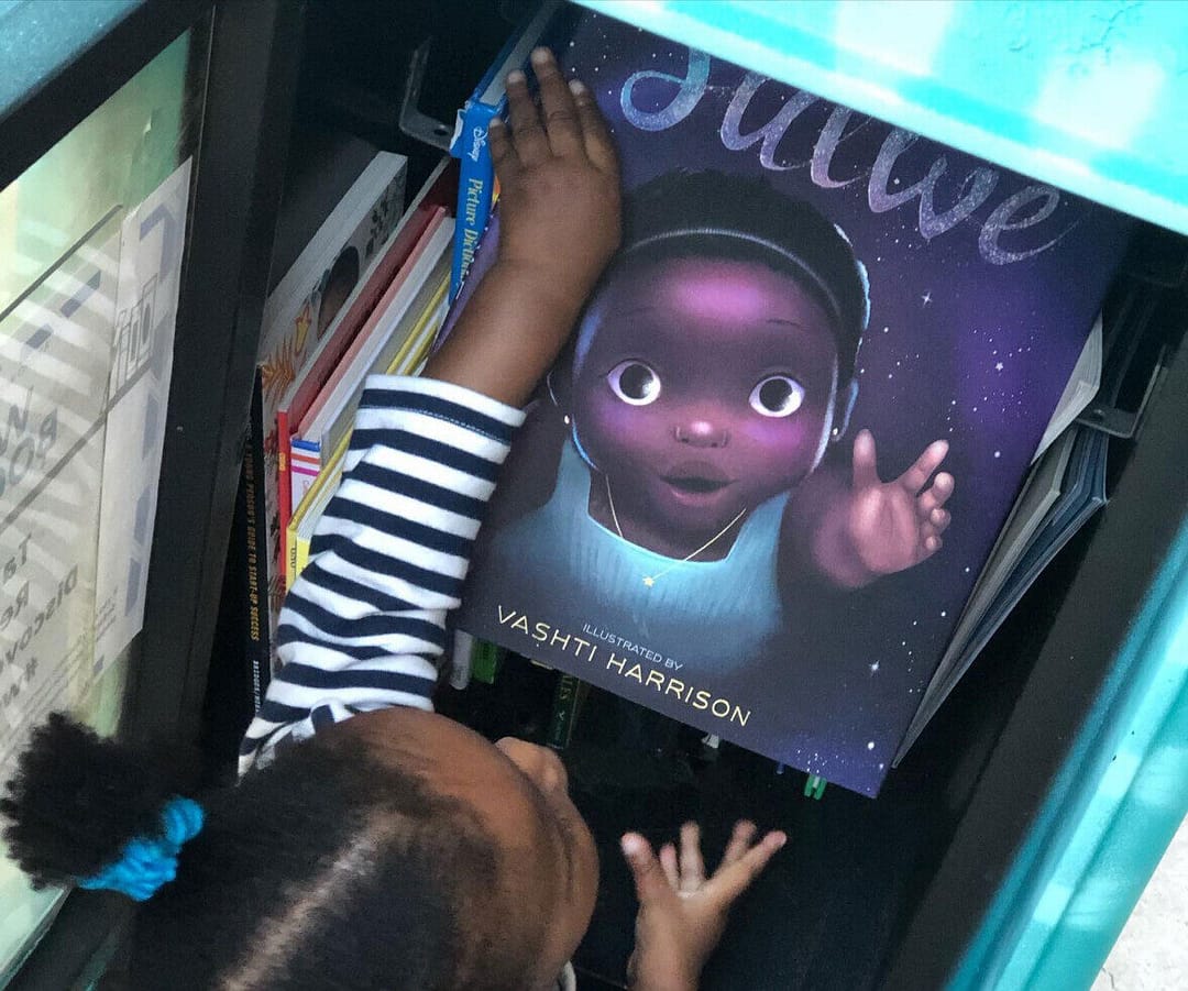 A young Black girl selects a book from Keep St. Pete Lit's WORK Book Box.