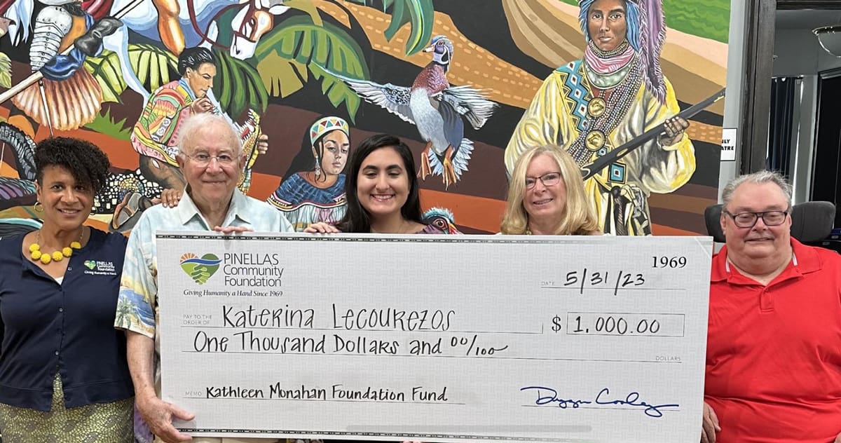 Pinellas Community Foundation director Leigh K. Davis and Kathleen Monahan Foundation Fund representatives Dave Wladaver, Kathleen Monahan, and Brian Orlick present Katerina Lecourezos, center, with an oversized check for the 2023 Kathleen Monahan Foundation Fund Scholarship at a grant presentation ceremony last month. Behind them is a mural at Tarpon Springs Cultural Center by Elizabeth Indianos depicting Native Americans and wildlife.