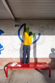Young male volunteer paints a mural on the wall.