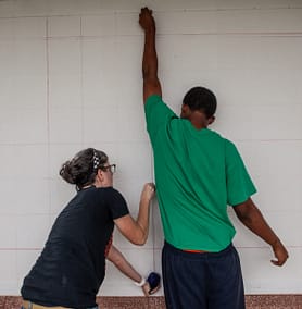 Carrie Boucher and volunteer make chalk lines on the wall for a mural.