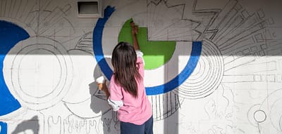 A young female volunteer paints a mural on the wall.