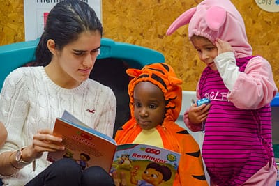 Preschool teacher reads to two students in costumes.