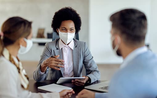 A professional advisor meets with clients in her office with masks on.