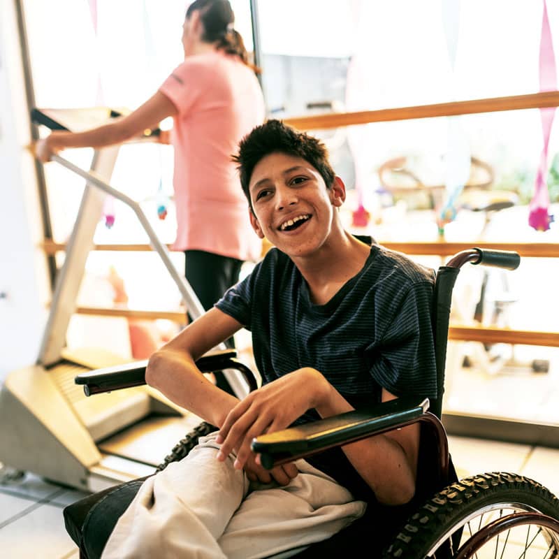 A boy in his wheelchair smiles while at the fitness center.