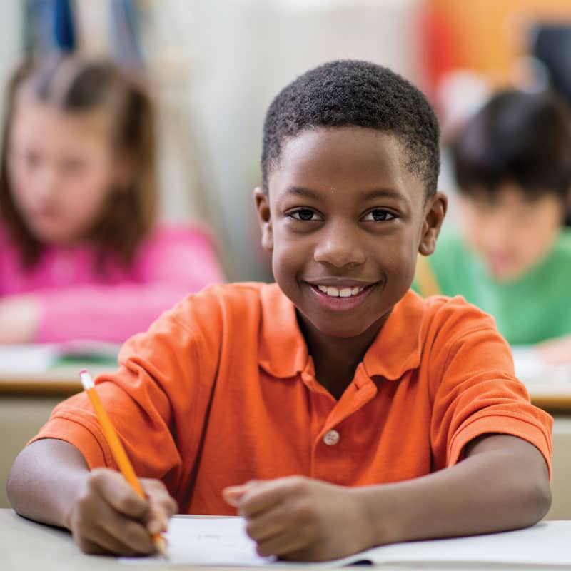 Black boy sits at classroom desk and writes.